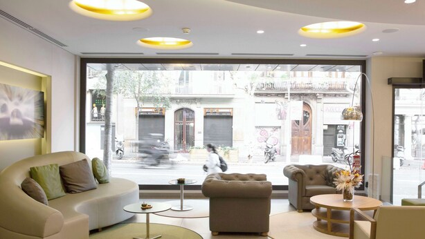 A modern hotel lobby with a sofa, ottoman, and round tables. - Best Western Premier Hotel Dante (Barcelona)