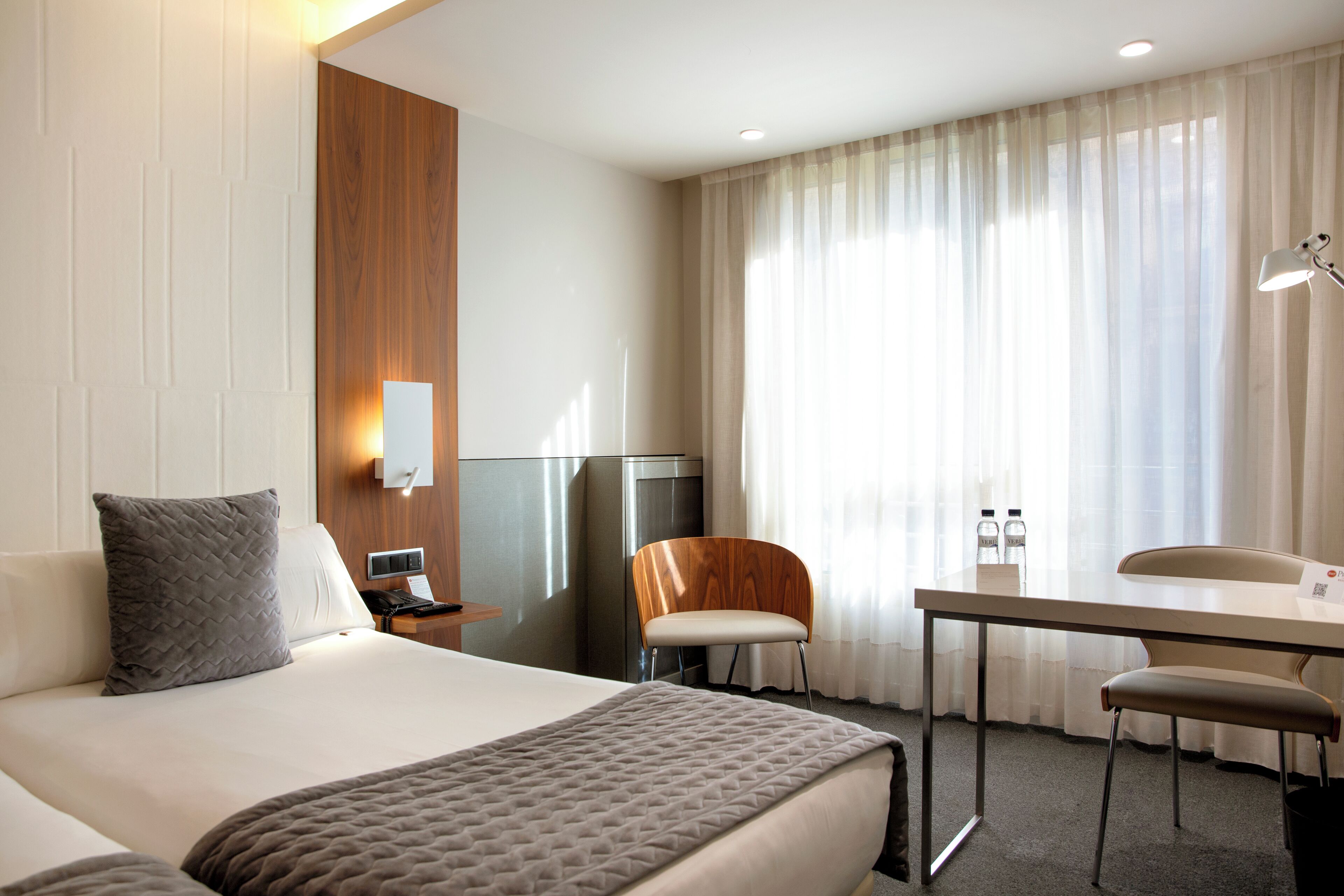 Una camera d'albergo con un letto grande, una scrivania, una sedia, una televisione e una finestra con tende.