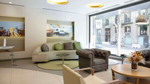 A modern hotel lobby with a sofa, armchairs, a round table, and a desk with a computer. - Best Western Premier Hotel Dante (Barcelona)