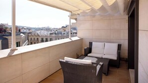 A balcony with a view of the city, a wicker sofa, and a tiled floor. - Best Western Premier Hotel Dante (Barcelona)