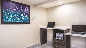 A business center with two desks, each with a laptop and a printer. A large abstract painting is on the wall.