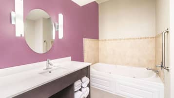 Un baño moderno con una pared morada, un lavamanos blanco, un espejo grande y una bañera blanca.