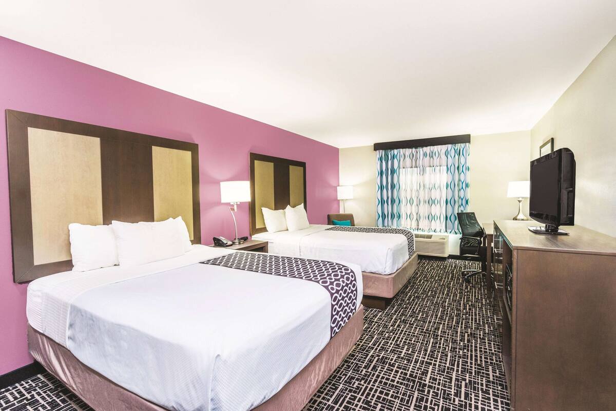 Una habitación de hotel con dos camas, un escritorio, un televisor y una ventana con cortinas.