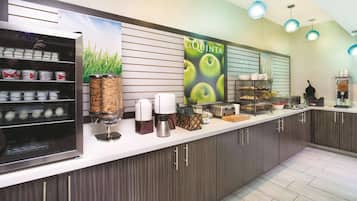 A modern kitchen with a coffee station, a refrigerator with food items, and a 'La Quinta' sign.