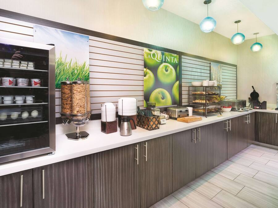 A modern kitchen with a coffee station, a refrigerator with food items, and a 'La Quinta' sign.