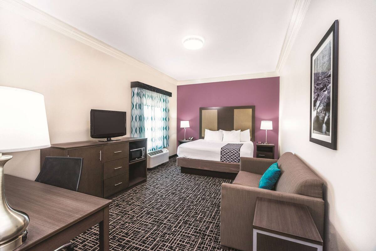 Una habitación de hotel con cama, escritorio, silla, televisor y sofá.