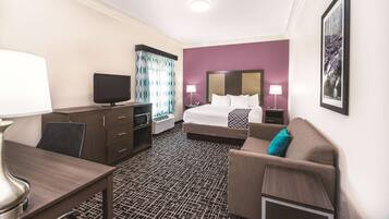 A hotel room with a bed, a desk, a chair, a TV, and a couch.