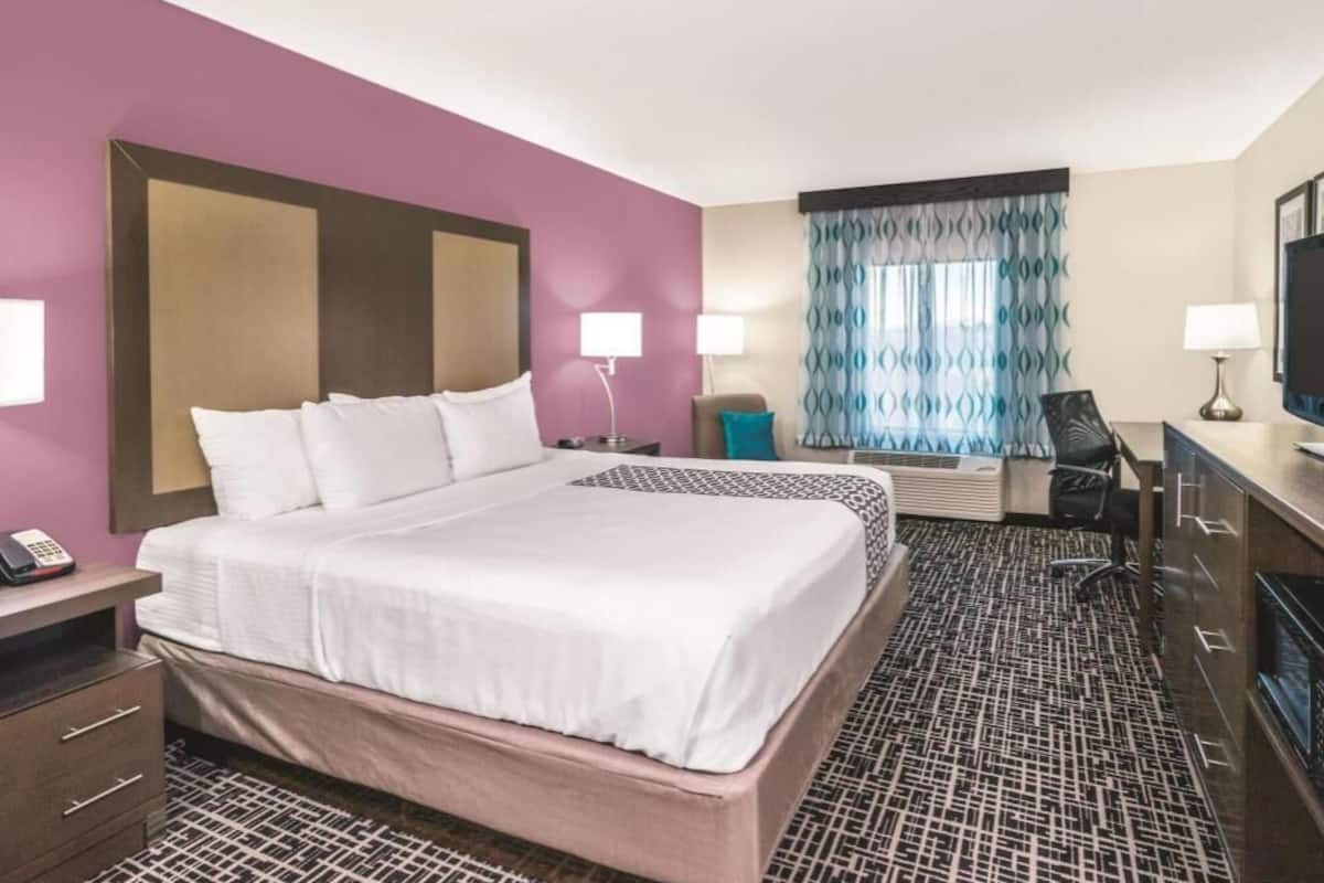 Habitación de hotel con una cama grande, mesitas de noche, un escritorio, una silla y una ventana con cortinas estampadas.