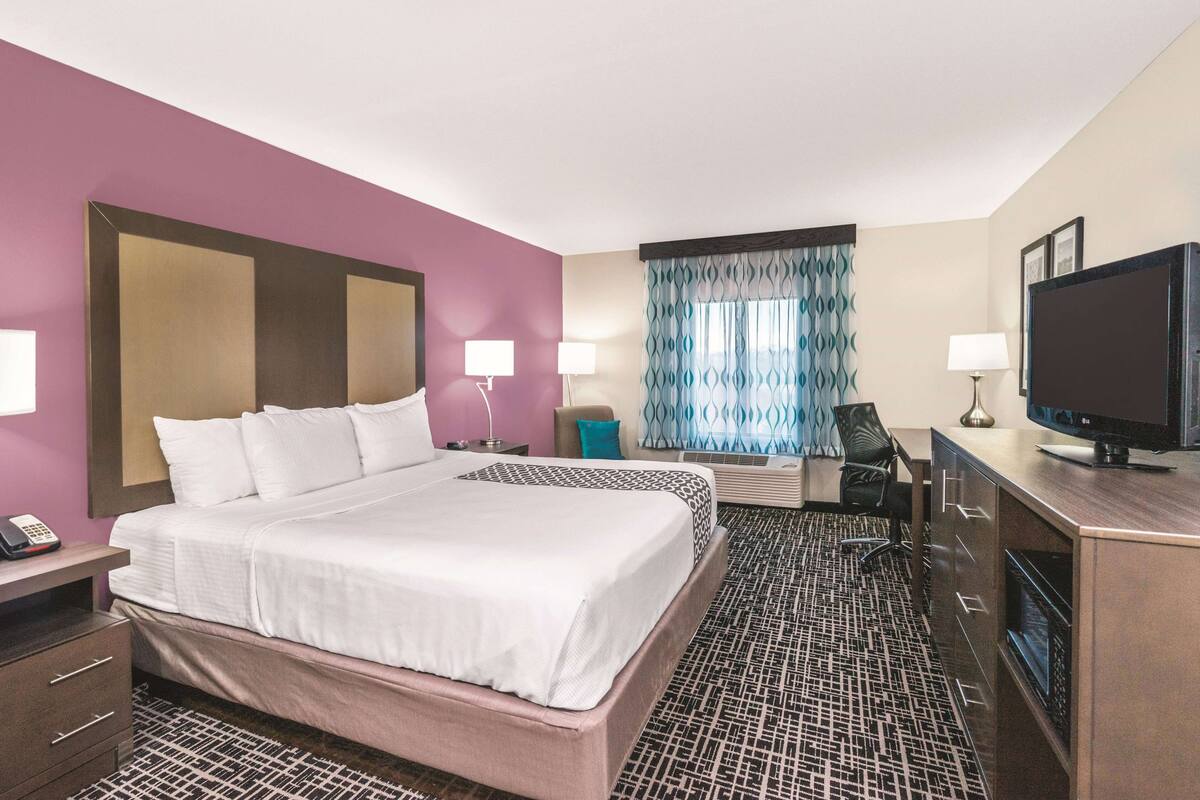 Una habitación de hotel con una cama grande, un escritorio con computadora, un televisor y una ventana con cortinas estampadas.
