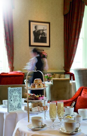 A tea service table with a tiered dessert display, tea cups, and glasses of champagne.