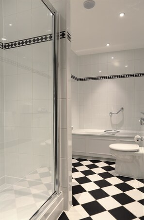 A bathroom with a checkered floor, a glass shower enclosure, a toilet, and a sink with a towel rack.