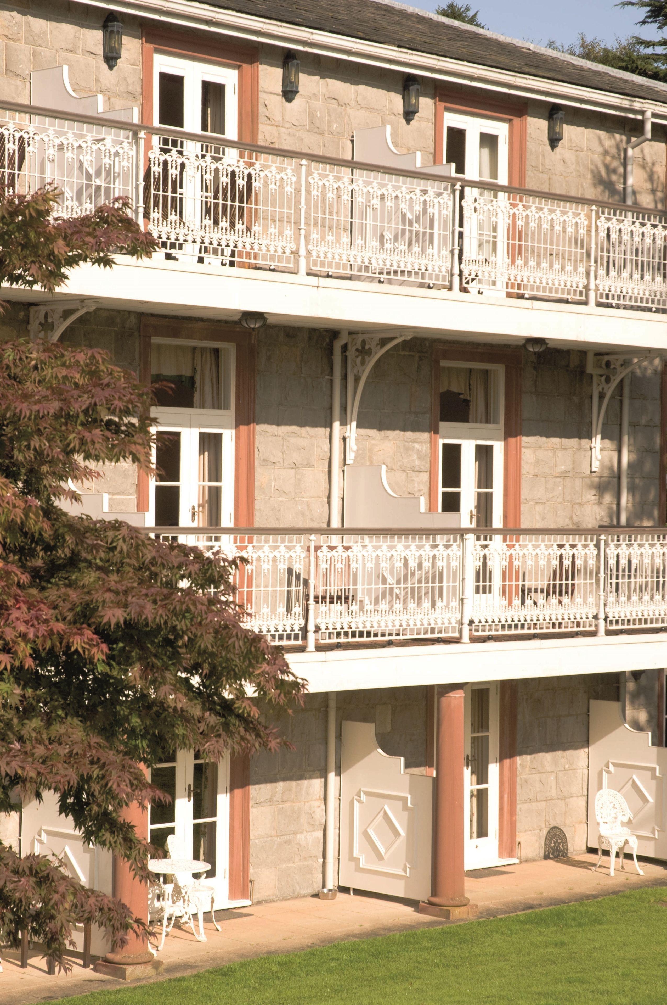 Un immeuble à plusieurs étages doté de balcons, d’une façade en pierre et d’un petit jardin agrémenté de chaises.