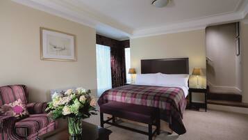 Una habitación de hotel con una cama grande, una silla, una mesita y un florero con flores.