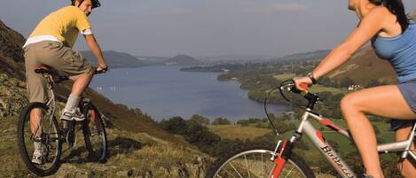 Dos personas en bicicleta contemplando un lago y colinas.