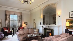 A traditional living room with a fireplace, patterned furniture, and a large mirror. - Macdonald Leeming House (Penrith)