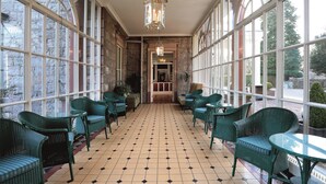 A sunlit room with large windows, green wicker furniture, and a tiled floor. - Macdonald Leeming House (Penrith)