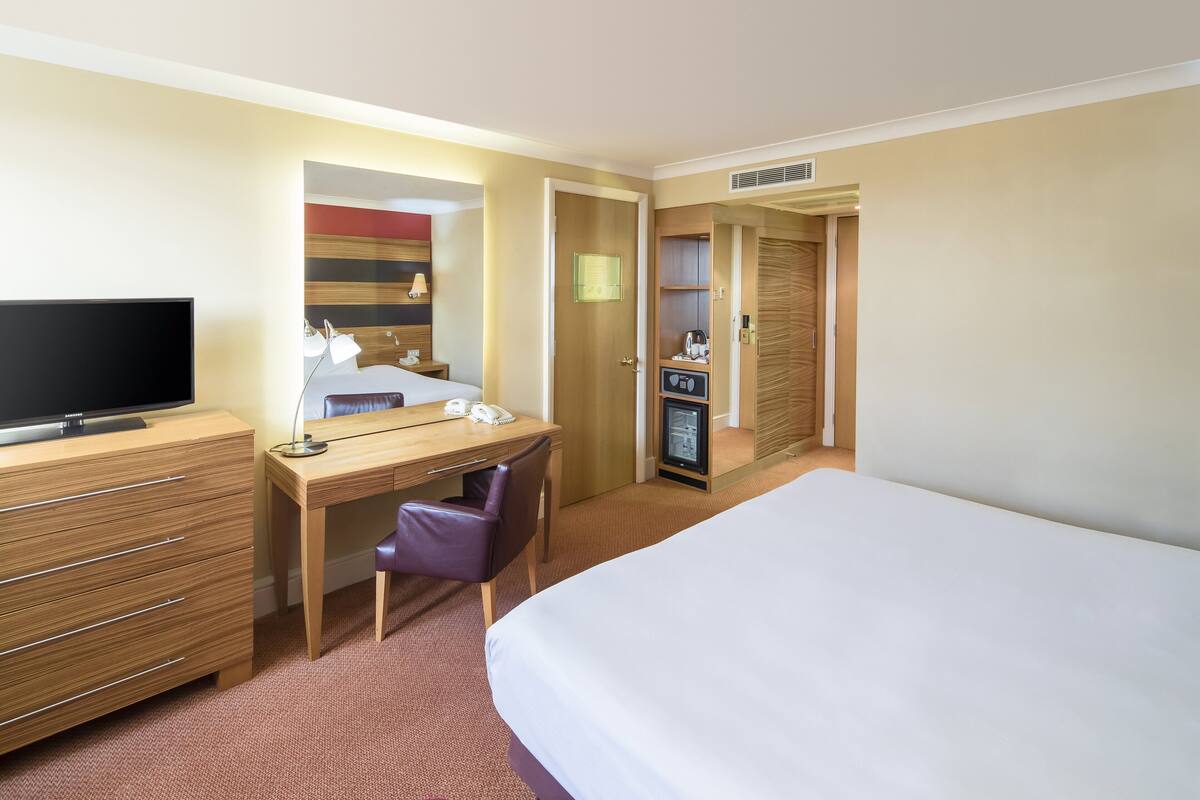 Une chambre d’hôtel comprenant un lit, un bureau avec une chaise, une télévision, un minibar et une armoire.