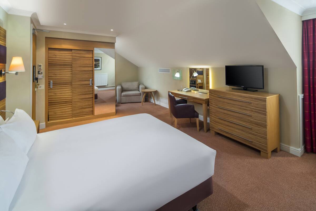 Une chambre d’hôtel avec un grand lit, un bureau avec une chaise, une télévision et une armoire.