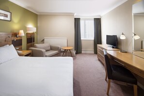 Hotellihuone, jossa on sänky, työpöytä, tuoli, televisio ja lamppu.