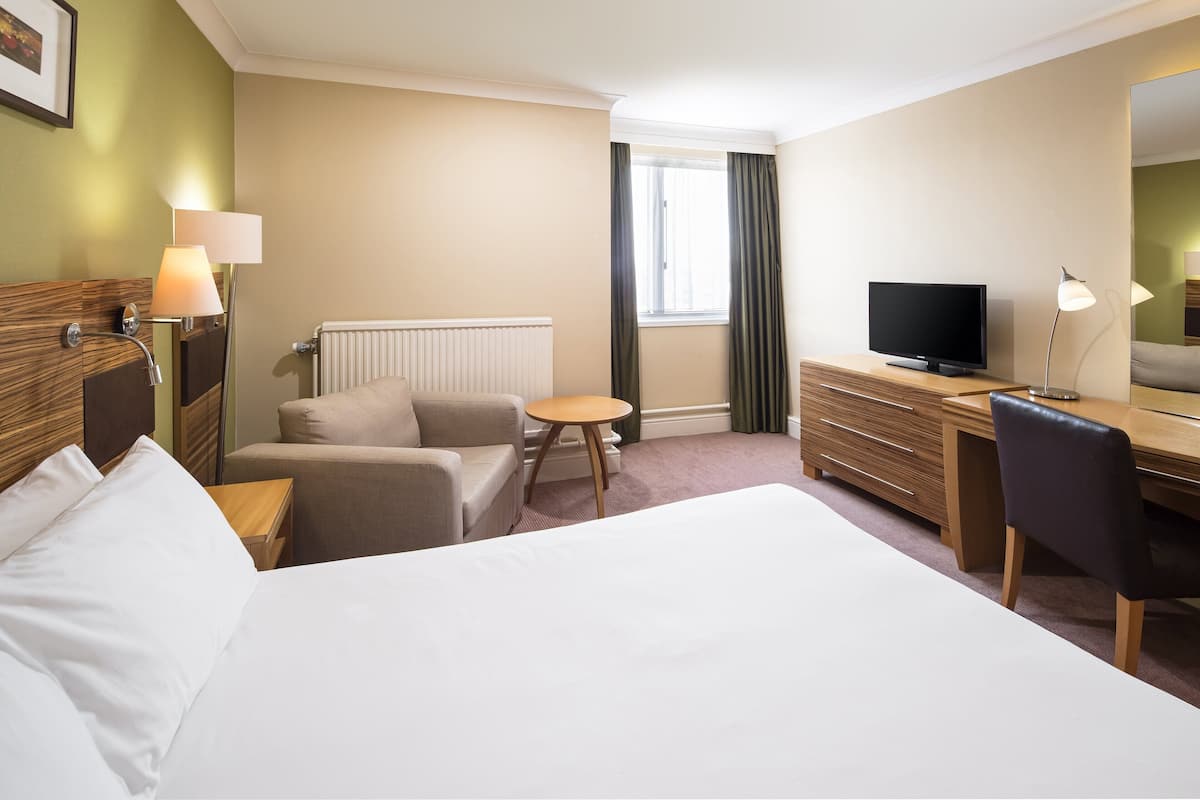 Une chambre d’hôtel avec un lit, un bureau, une chaise, une télévision et une fenêtre avec des rideaux.