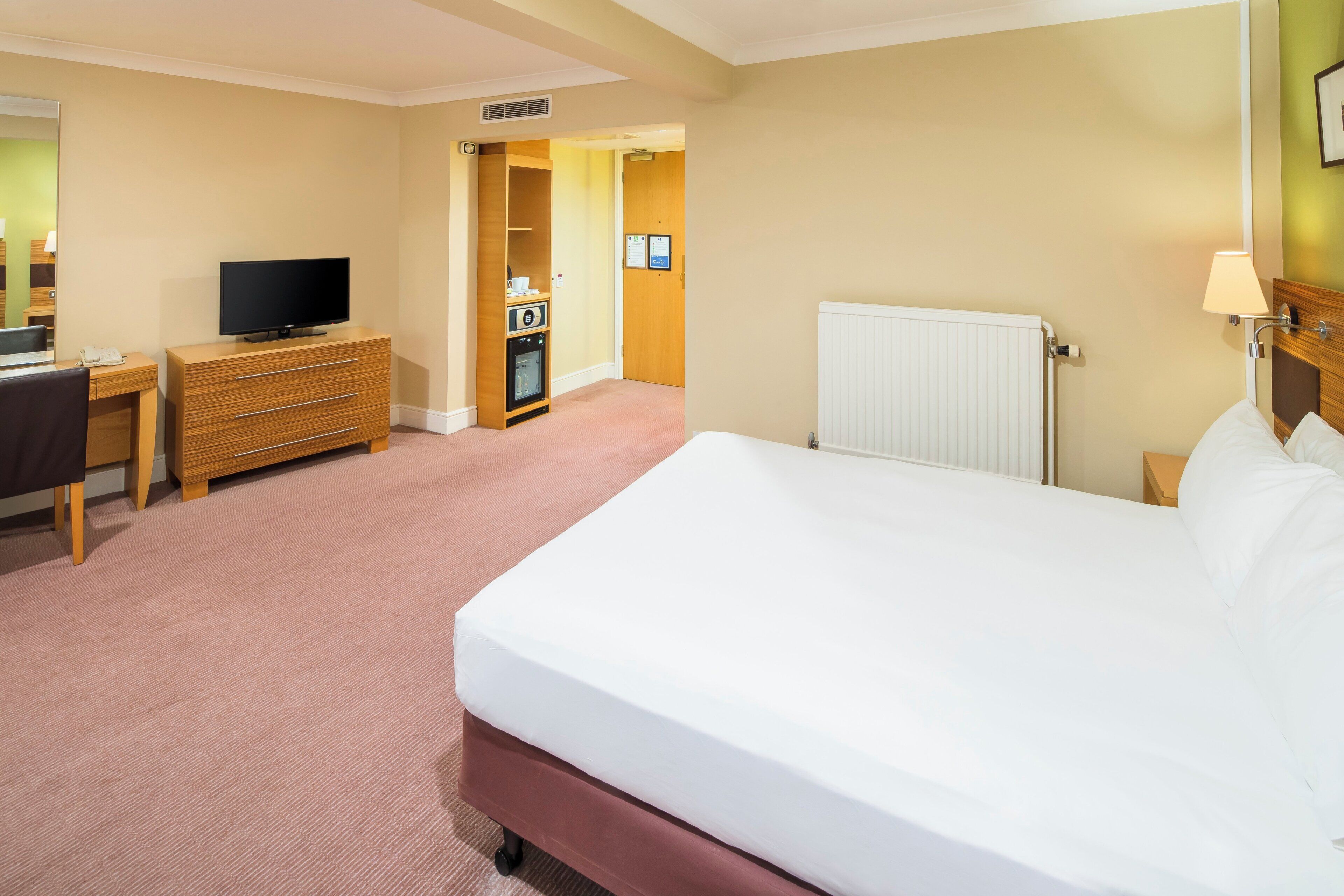Ein Hotelzimmer mit Bett, Schreibtisch, Fernseher, Kommode und Heizkörper.