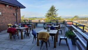 An outdoor patio with multiple tables and chairs, a brick wall, and a view of the landscape. - Crowne Plaza Chester by IHG (Chester)