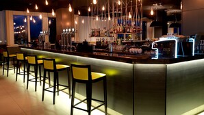 A bar area with multiple stools, a bar counter, and a variety of bottles and glasses. - Crowne Plaza Chester by IHG (Chester)