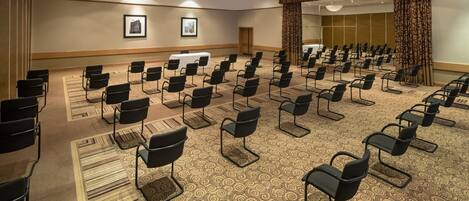 A conference room with rows of chairs, a carpeted floor, and framed pictures on the walls.