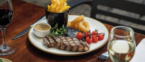A plate of grilled steak, cherry tomatoes, grilled onions, and French fries on a wooden table.