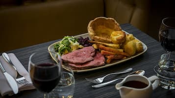 A dining table with a plate of food, including roast beef, Yorkshire pudding, and vegetables, along with a glass of red wine and a cup of tea.