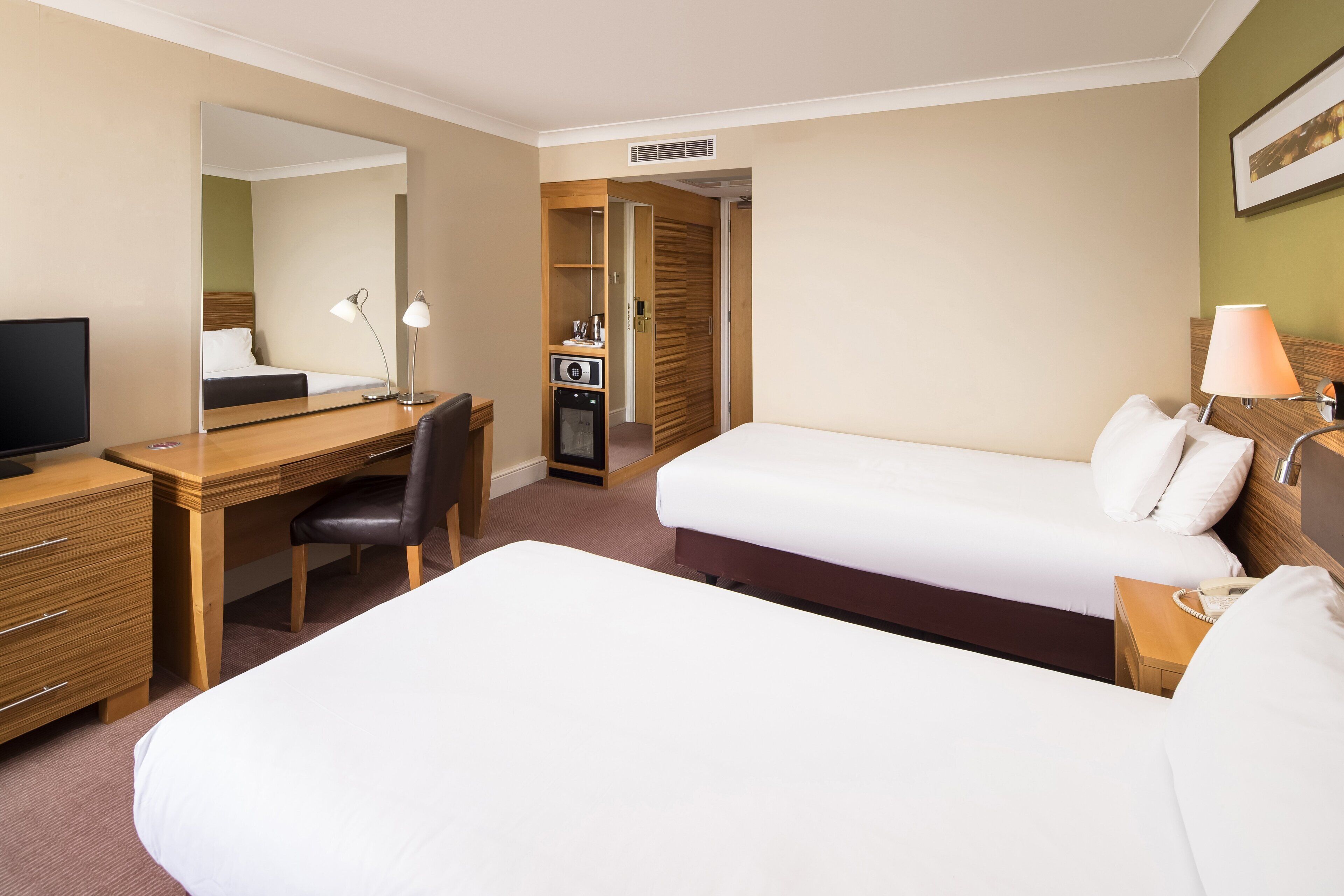 Una habitación de hotel con cama, escritorio, silla, televisión, lámpara y armario.
