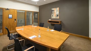 Una sala conferenze con un grande tavolo in legno, sedie nere, bottiglie d'acqua e un quadro appeso al muro.