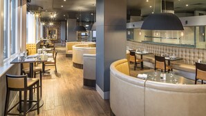 A modern restaurant with leather seating, wooden tables, and a brick accent wall. - Crowne Plaza Chester by IHG (Chester)