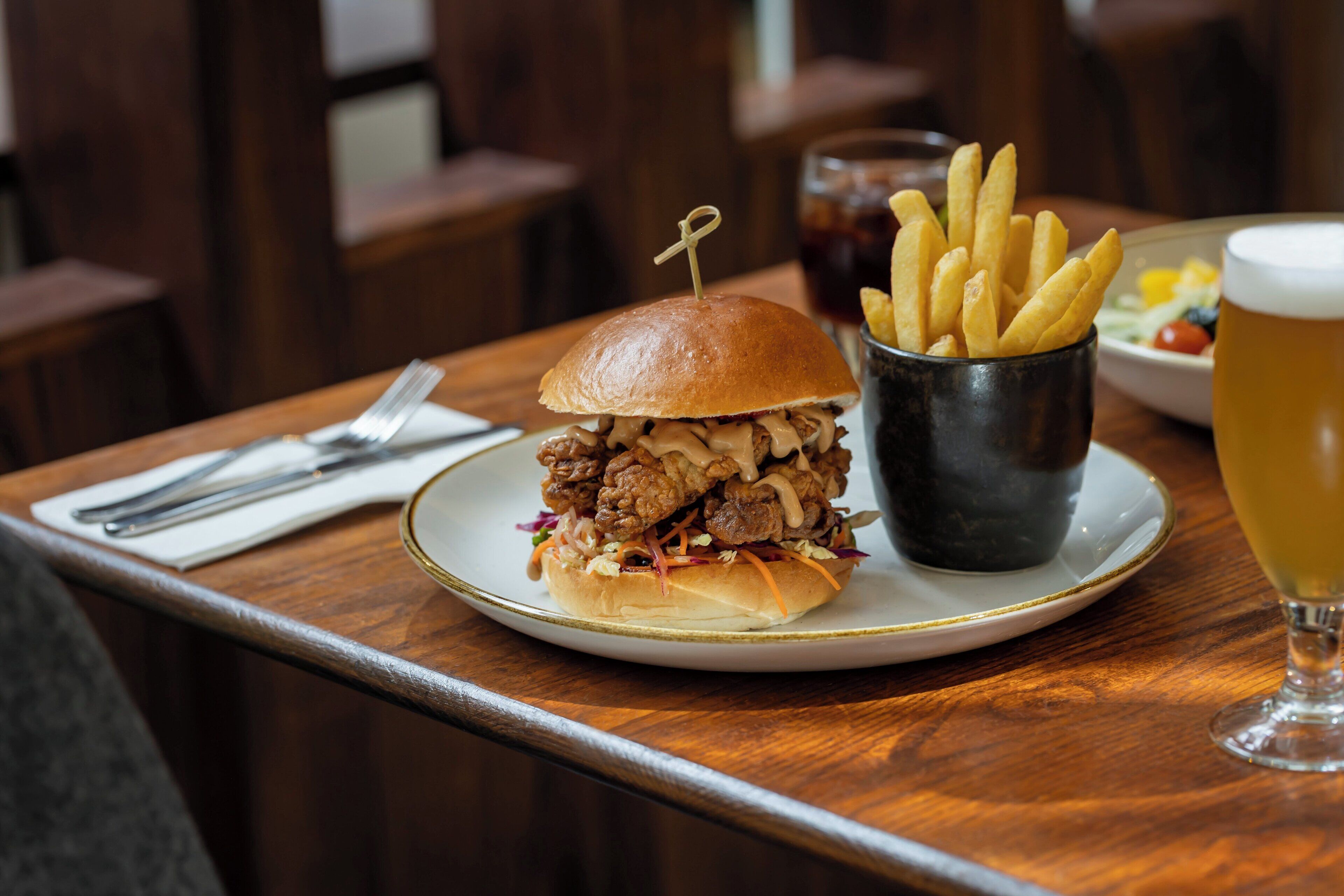 A sandwich with fries and a glass of beer on a wooden table.
