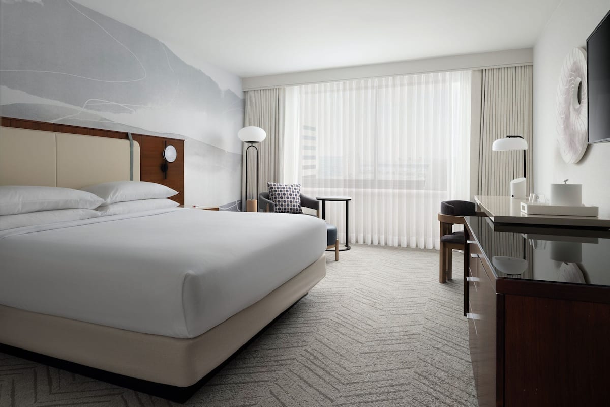 Une chambre d’hôtel avec un grand lit, un bureau, une chaise, une petite table et un téléviseur fixé au mur.