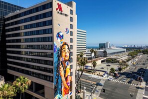 A modern hotel with a large mural on the side, a clear view of the street below, and a parking lot in the foreground.