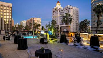 An outdoor patio with tables and chairs, a pool, and a view of surrounding buildings.