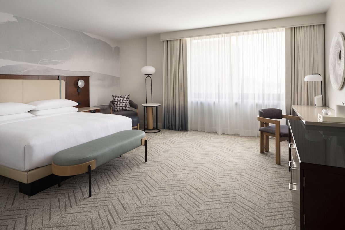 Une chambre d’hôtel moderne, dotée d’un grand lit, d’un bureau, d’une chaise, d’une petite table et d’une lampe.