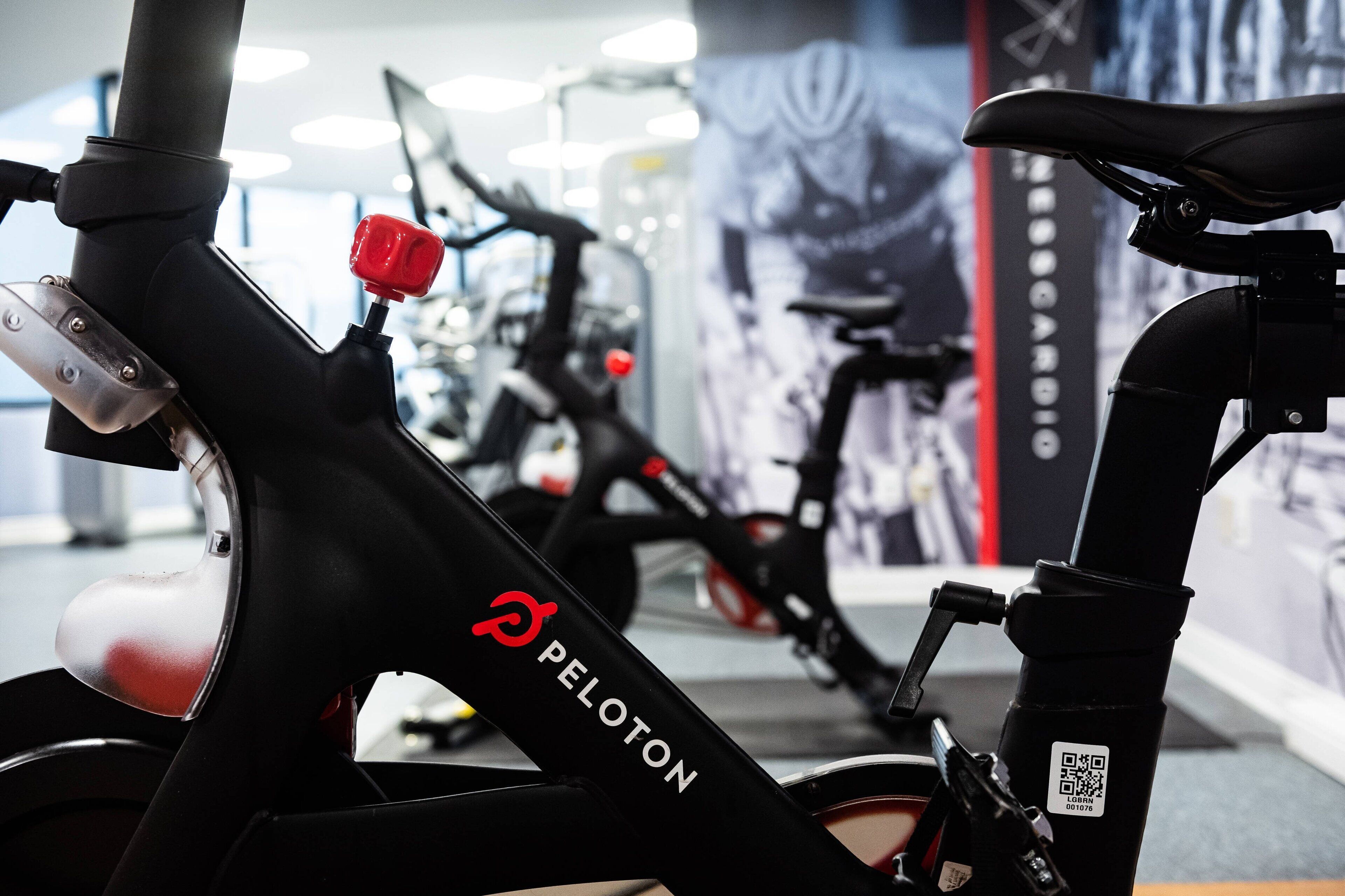 Een hometrainer met een rode stuurstang en de merknaam 'Peloton' op het frame.