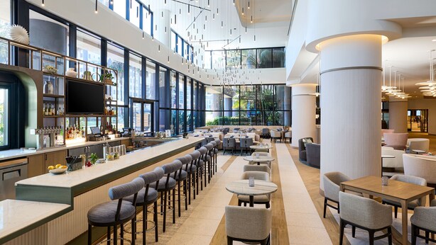 A modern bar area with high ceilings, large windows, and a variety of seating options including bar stools and tables. - Marriott Long Beach Downtown (Long Beach)