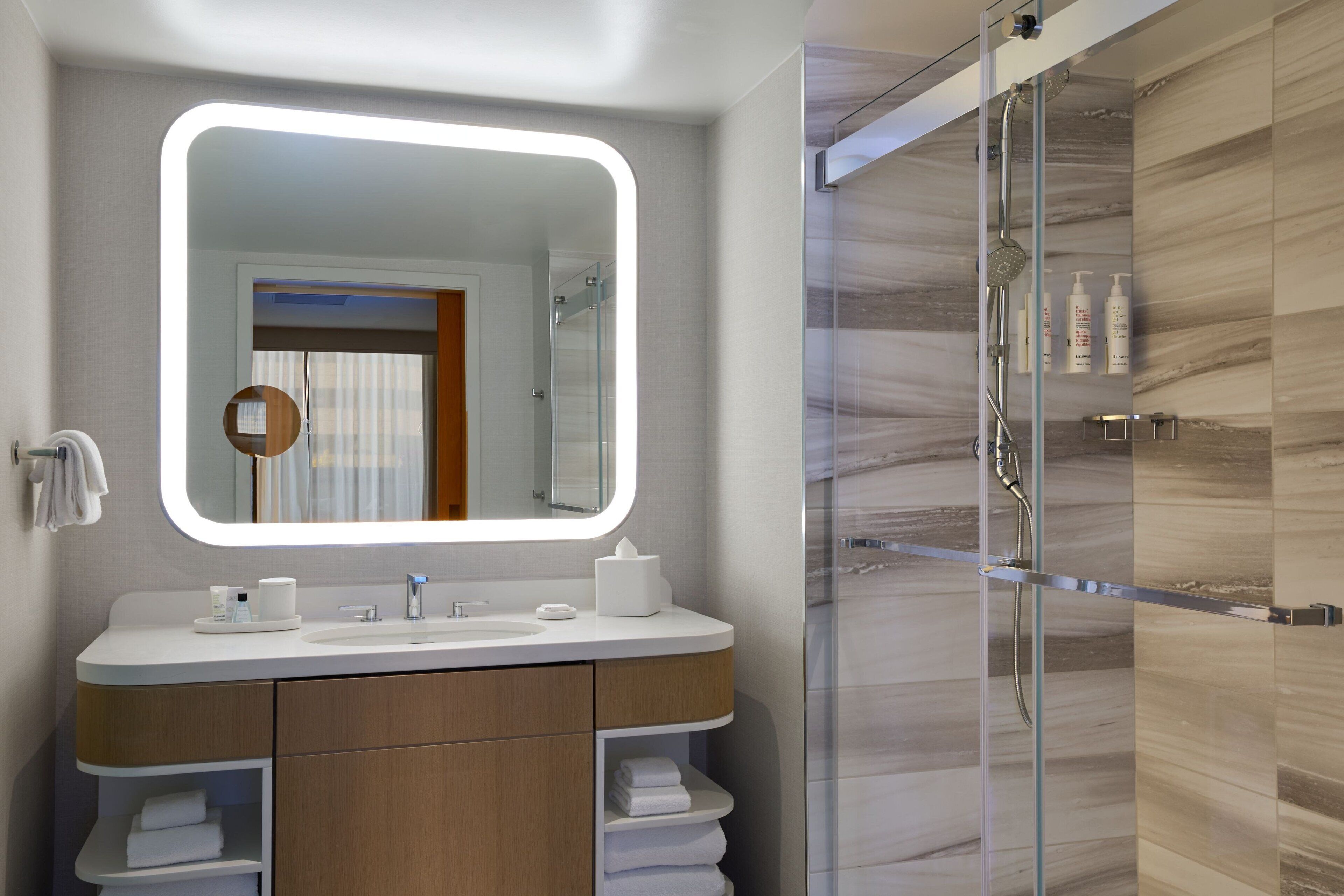 Une salle de bain moderne avec un grand miroir, une douche en verre et un meuble-lavabo avec des serviettes.