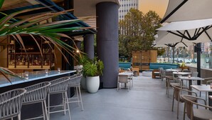 An outdoor seating area with a bar, potted plants, and a view of the cityscape. - Marriott Long Beach Downtown (Long Beach)