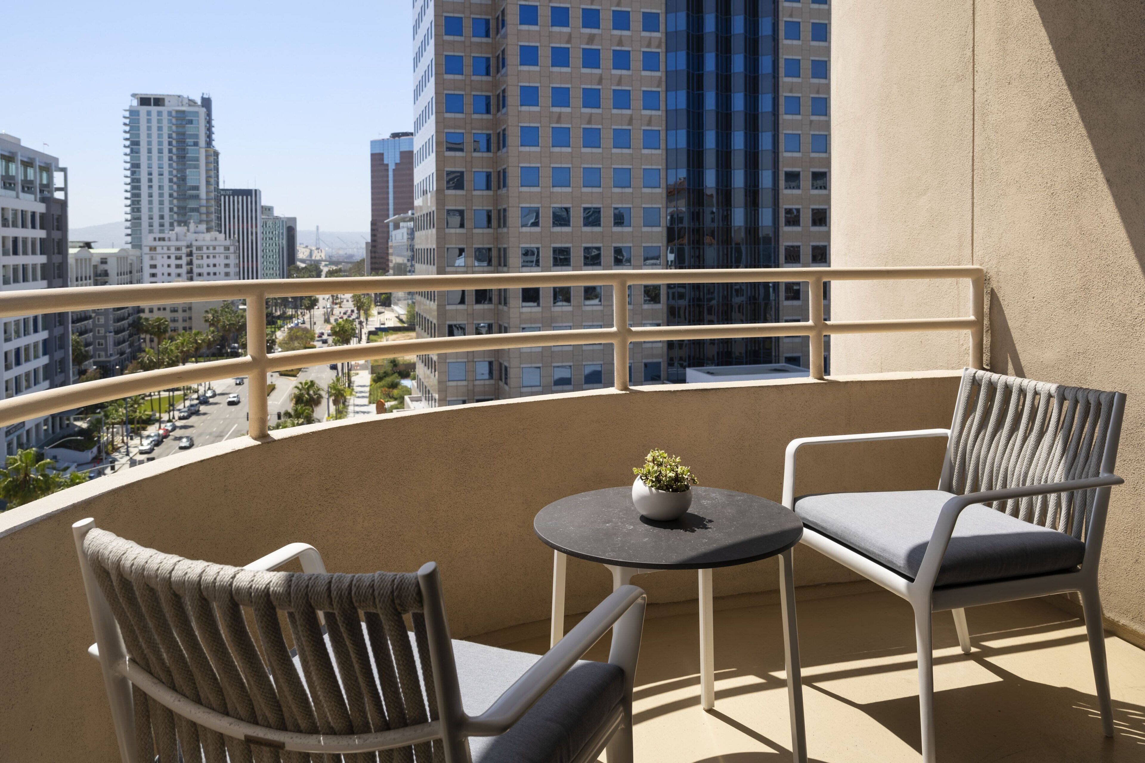 A balcony with two chairs and a small table, overlooking a cityscape with tall buildings.