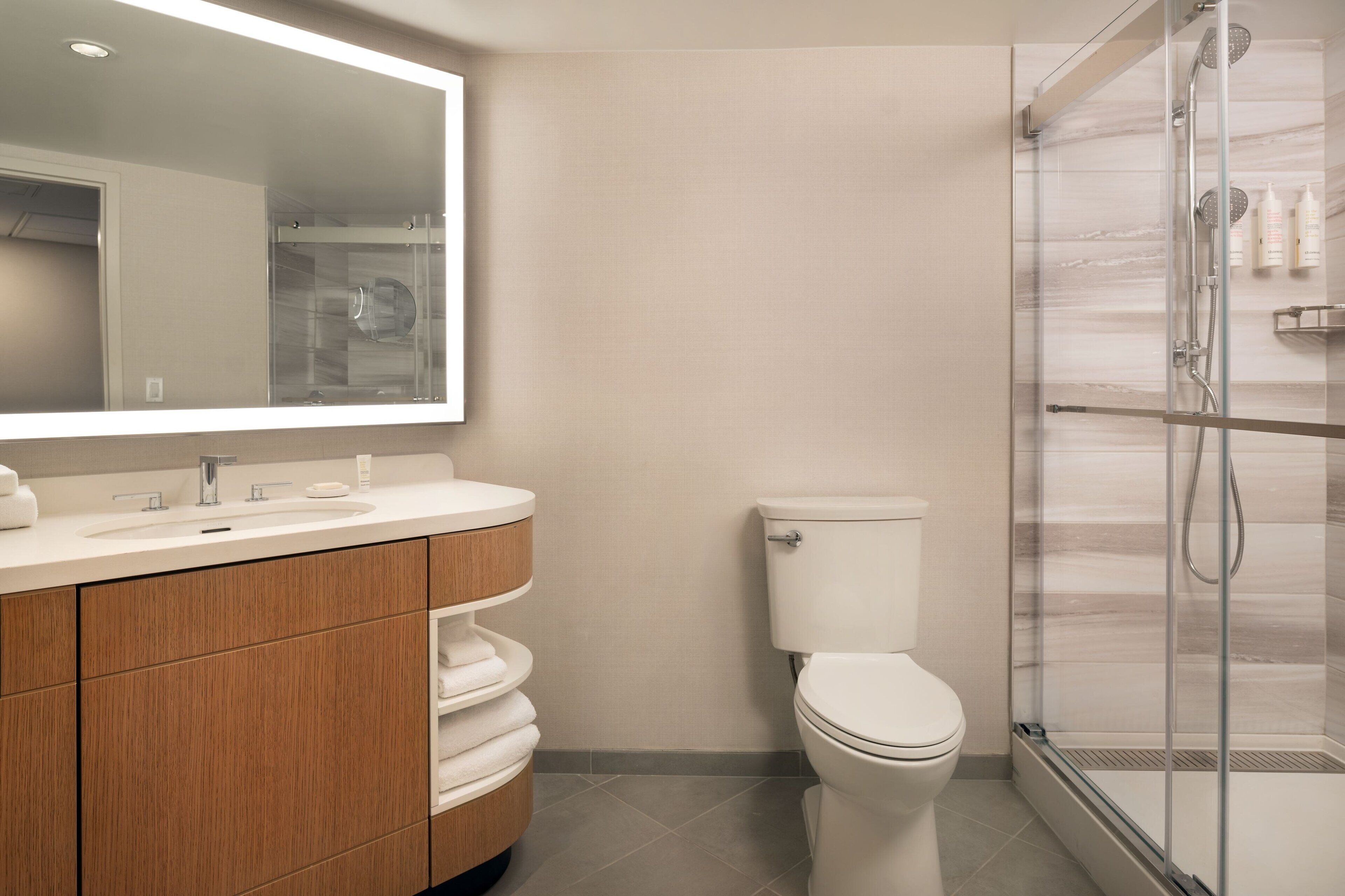 A modern bathroom with a glass shower enclosure, a white toilet, and a wooden vanity with a mirror.