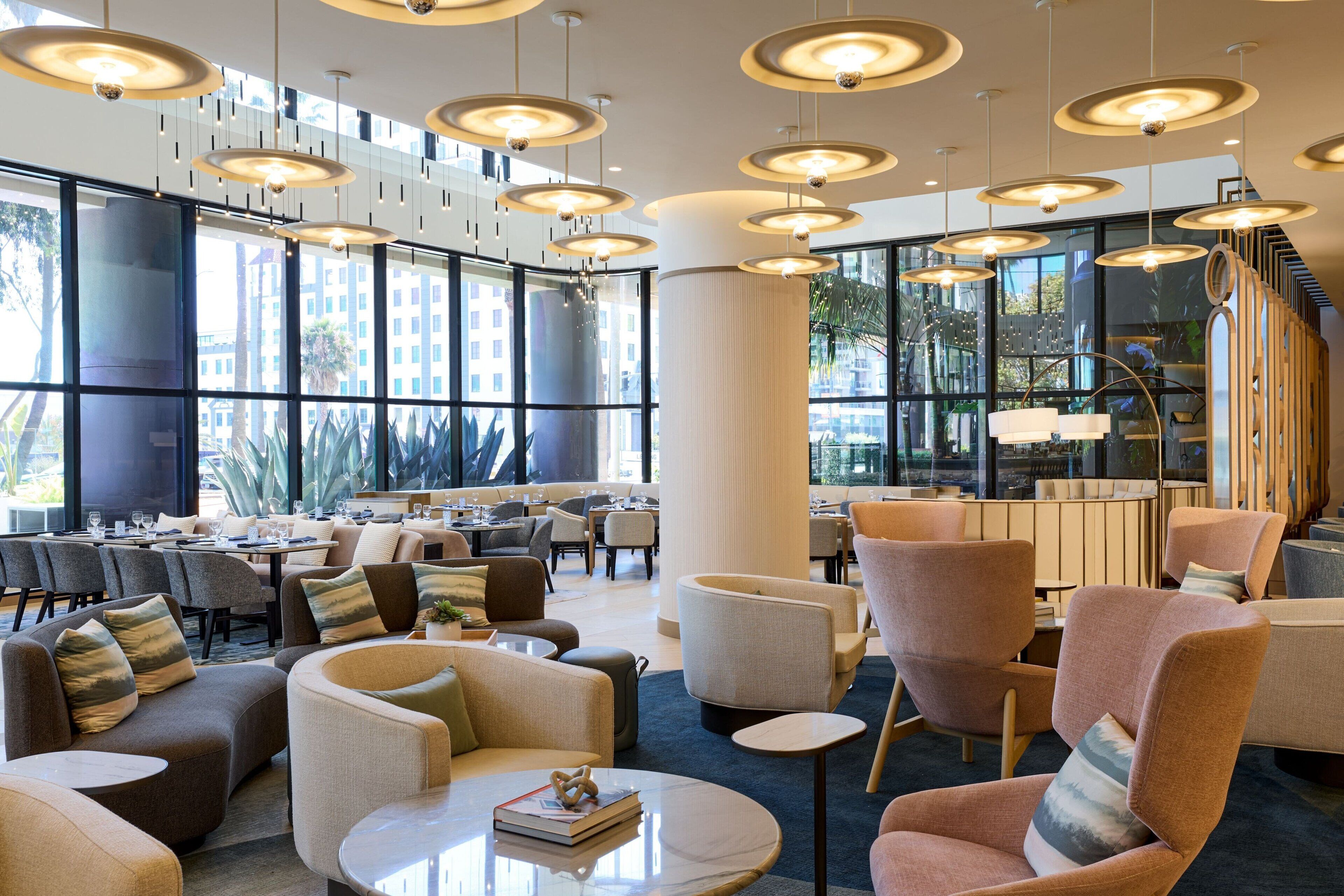 Un moderno vestíbulo de hotel con varias zonas de estar, ventanas amplias e iluminación contemporánea.