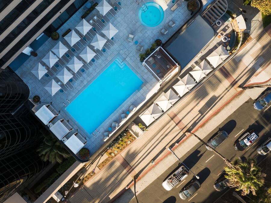 An aerial view of a hotel with a swimming pool, lounge area, and a street with cars.