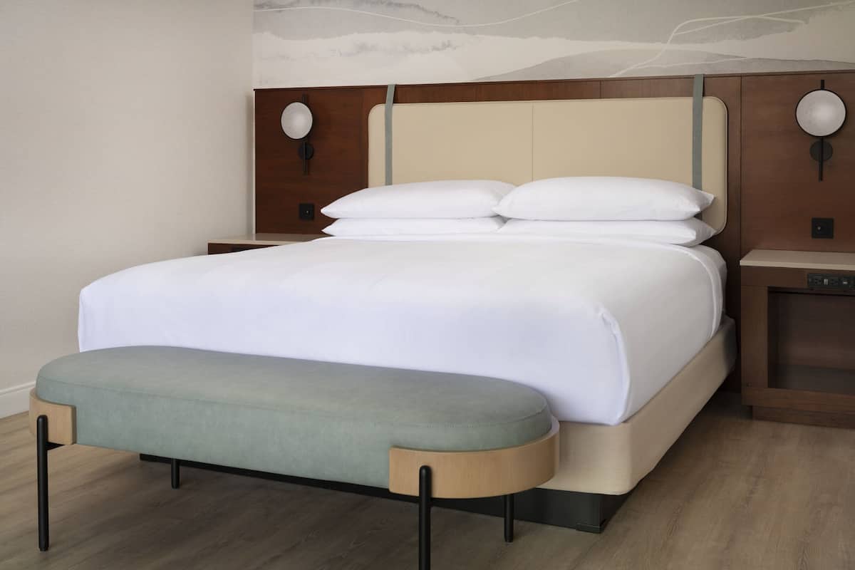 Un lit bien fait, avec une tête de lit en bois, une table de chevet avec une lampe et un banc au pied du lit.