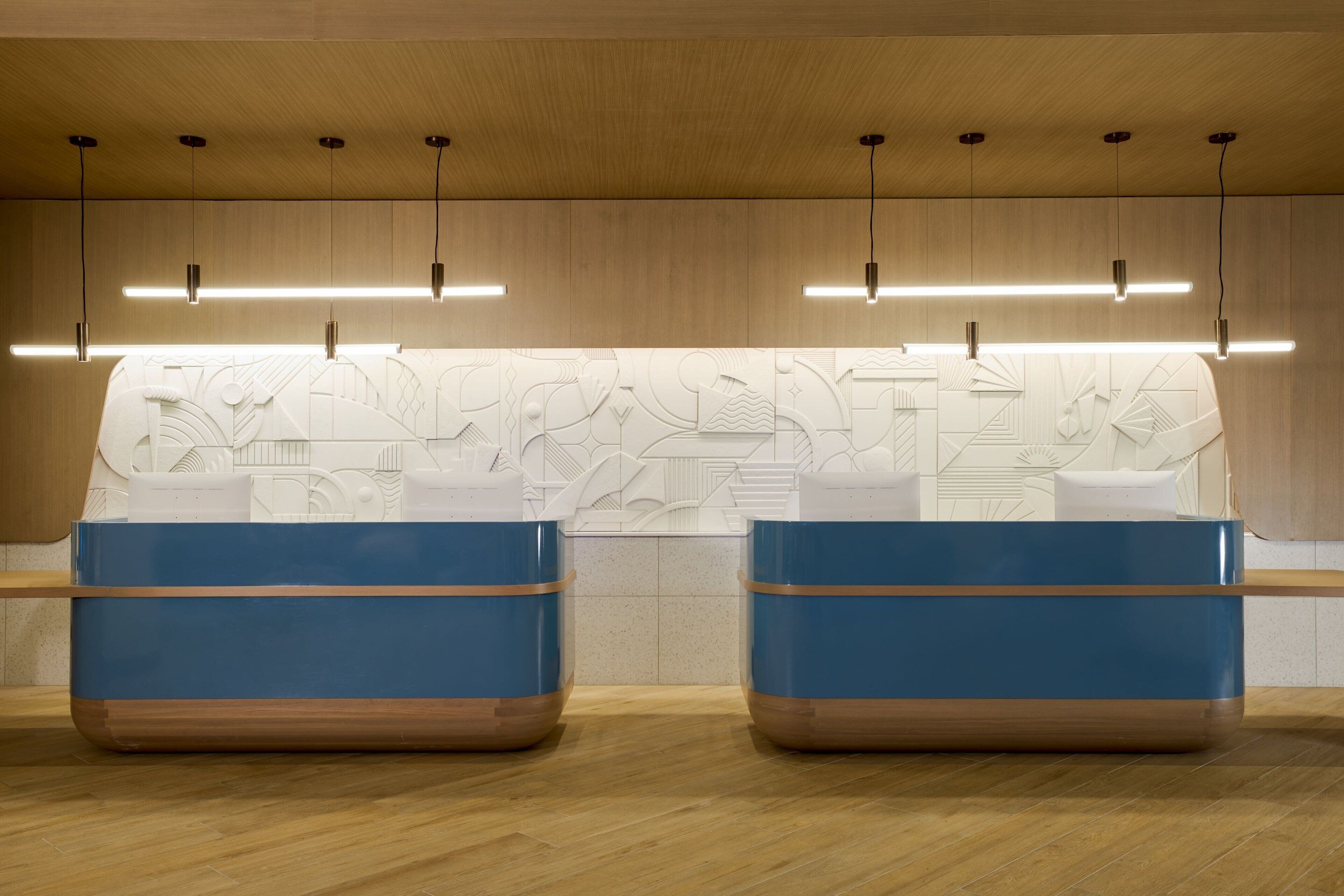 Une salle de bain moderne avec deux lavabos bleus, un plancher en bois et un motif géométrique sur le mur.