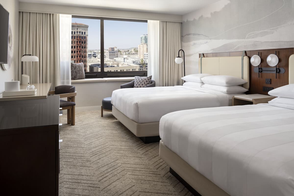 Une chambre d’hôtel avec deux lits, un bureau, une chaise, une lampe et une vue sur le paysage urbain.
