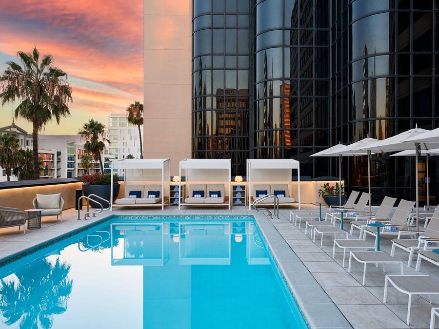 A rooftop pool area with lounge chairs and umbrellas, surrounded by modern buildings.